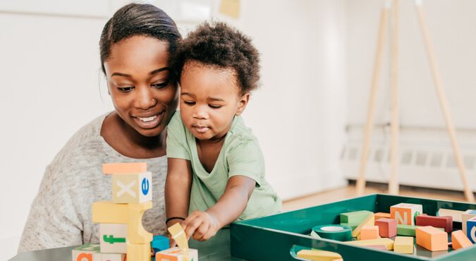 Mãe e bebê brincam felizes com blocos de montar, em artigo sobre visão do bebê. Ambos são negros e vestem roupas claras