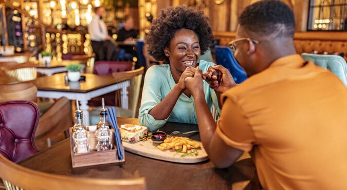 Casal de homem e mulher felizes jantando em restaurante durante vale night para os pais. Ambos são negros e usam roupas claras