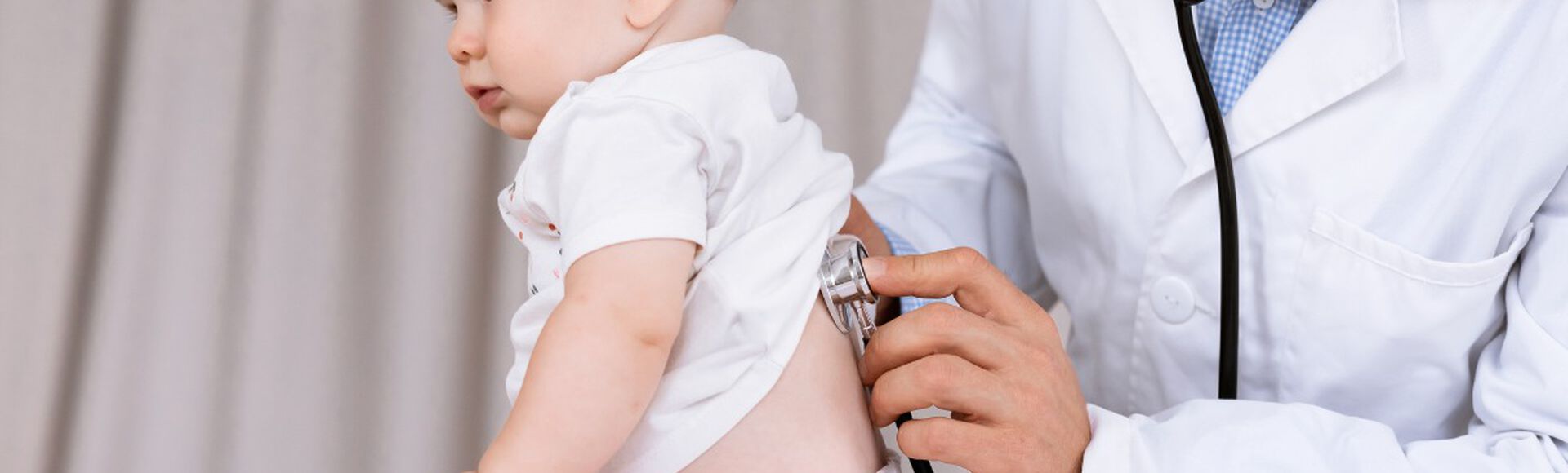 médico usando um estetoscópio para examinar um bebê sentado em uma mesa de exame.