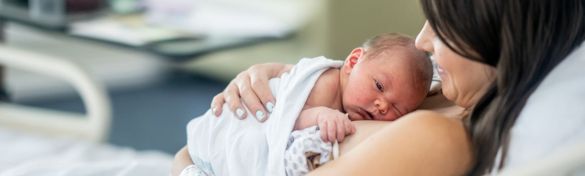 Mamãe e bebê recém-nascido em posição de método canguru. Ambos são brancos e estão deitados na cama do hospital