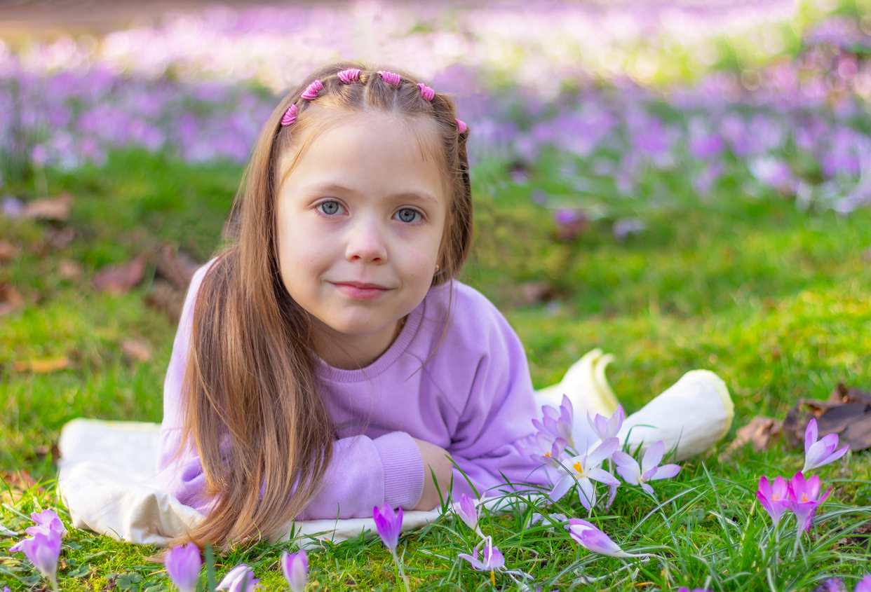 Menina deitada na grama com penteado infantil.