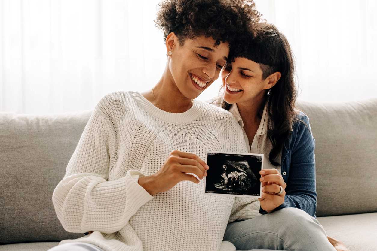 Casal vendo juntas o exame de sexagem do bebê que uma das mães está esperando. Estão felizes.