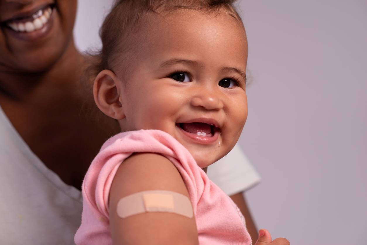 Bebê sorrindo com curativo no braço após vacinação.