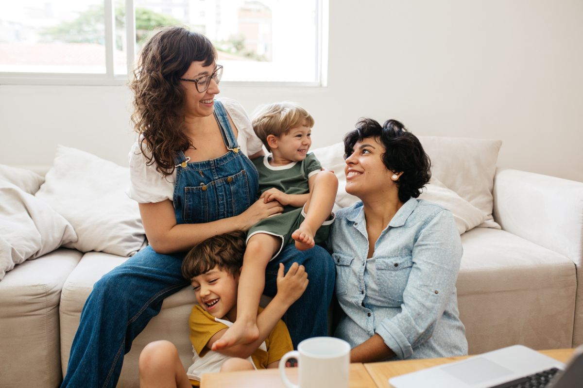 família feliz sentada em um sofá em uma sala de estar. A família inclui duas mães e dois filhos pequenos.