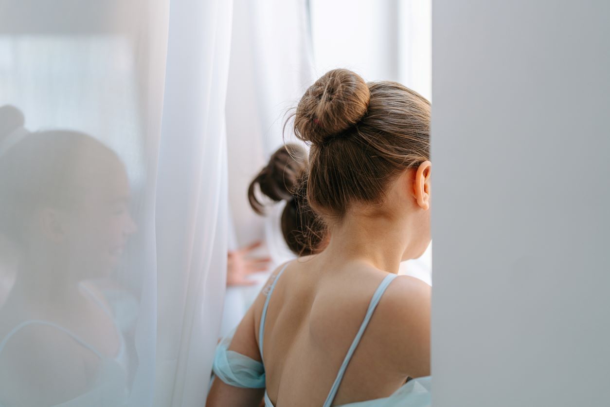 Menina com penteado infantil de coque olhando pela janela.