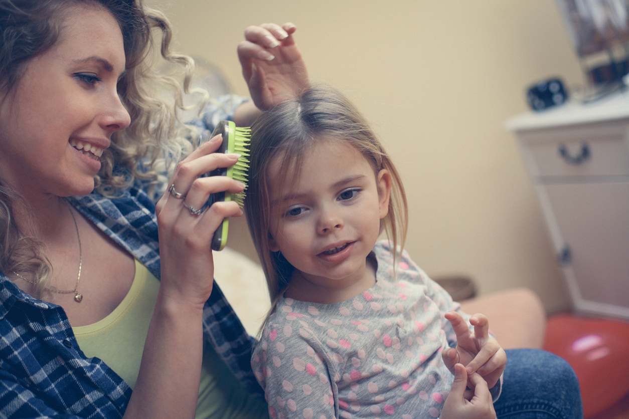 Mãe usando escova para pentear o cabelo embolado da filha.