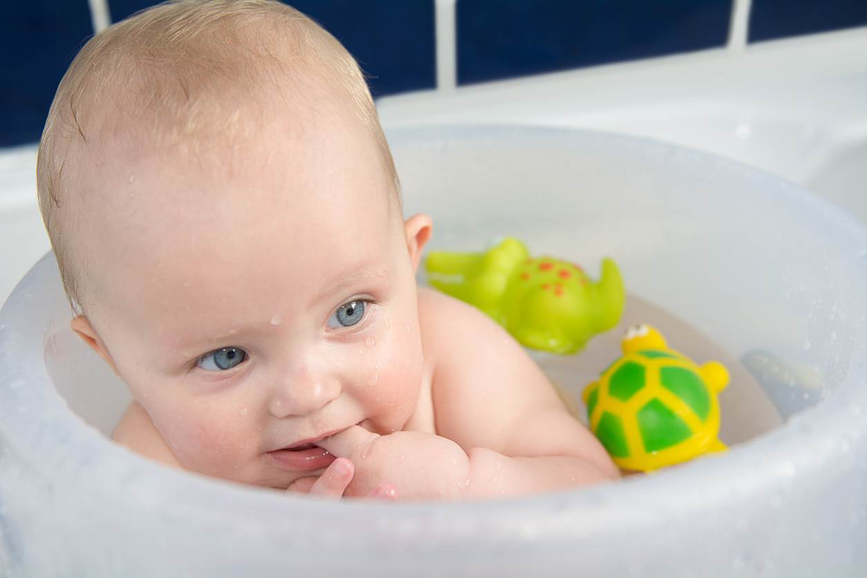 Bebê dentro de uma banheira brincando com brinquedos de borracha.