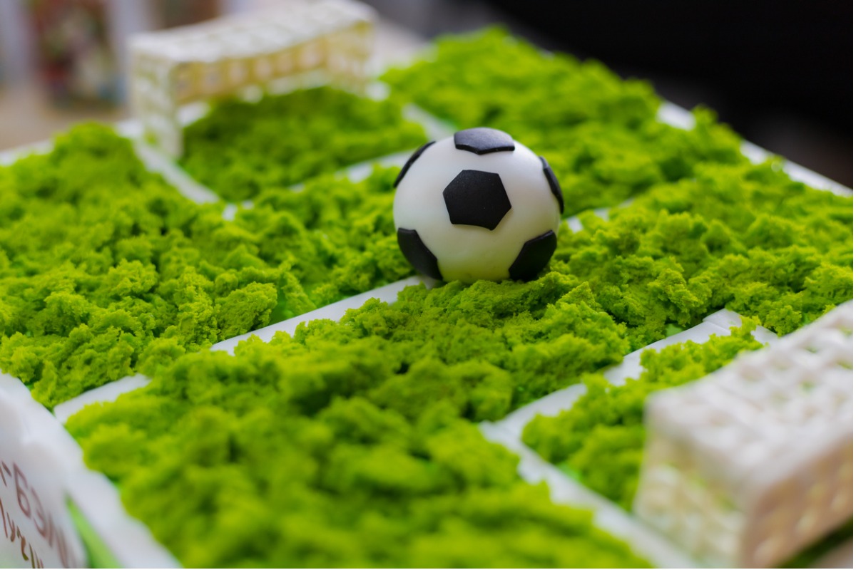 Imagem de um bolo em formato de campo de futebol em miniatura feito de grama artificial. 