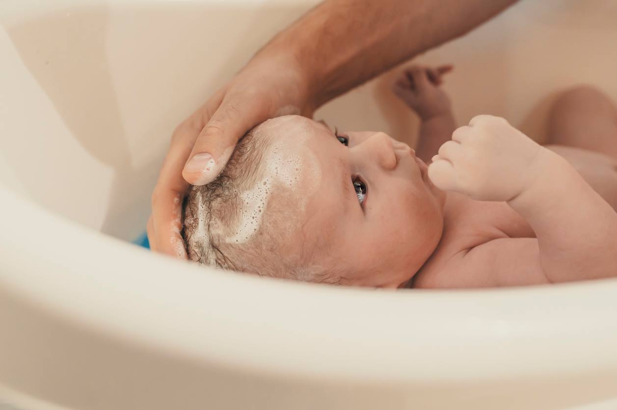 Vebê sendo cuidadosamente lavado na banheira por adulto.