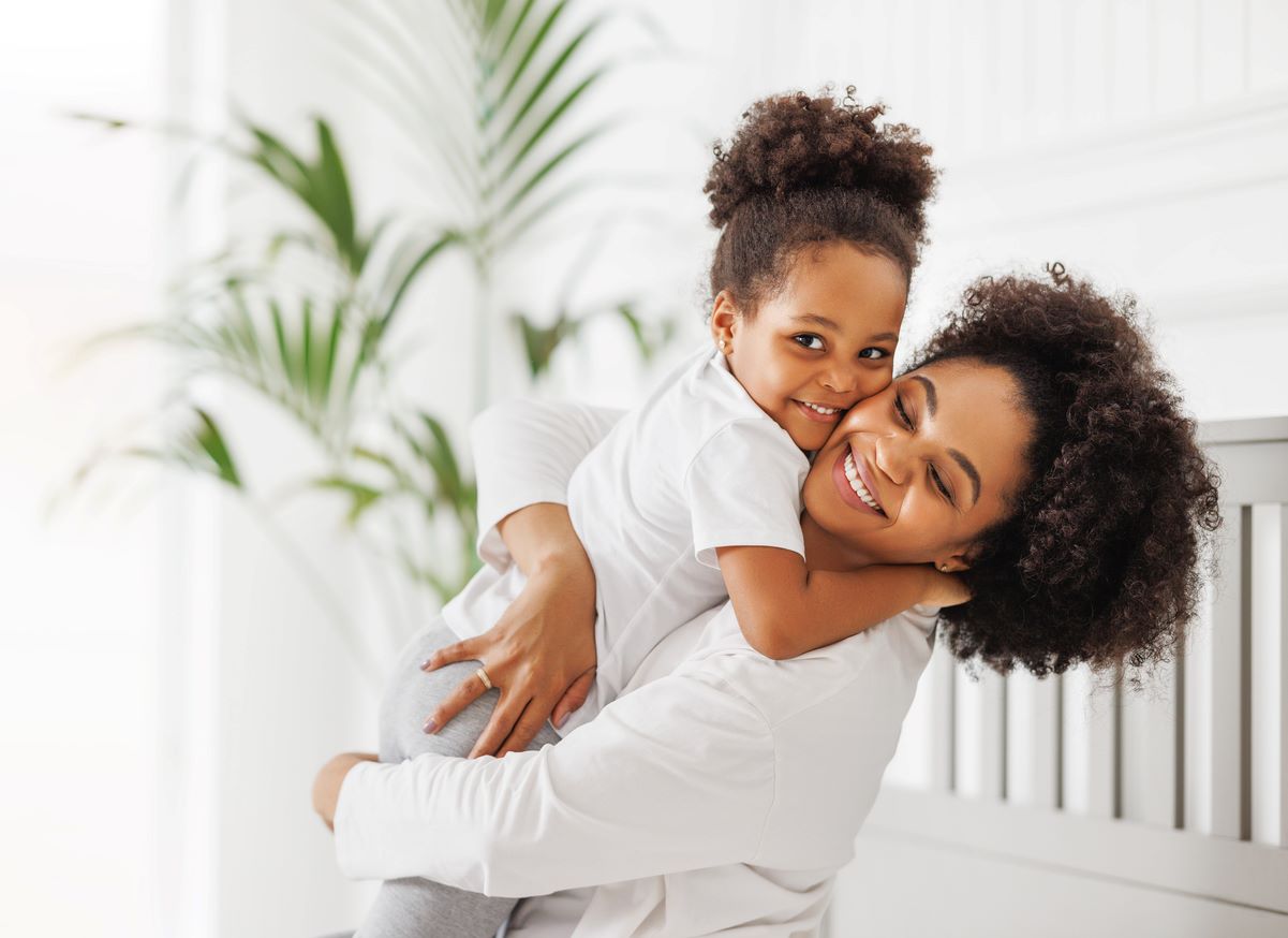 Mãe e filha abraçadas, esbanjando belos cabelos crespos, penteados de forma distinta 