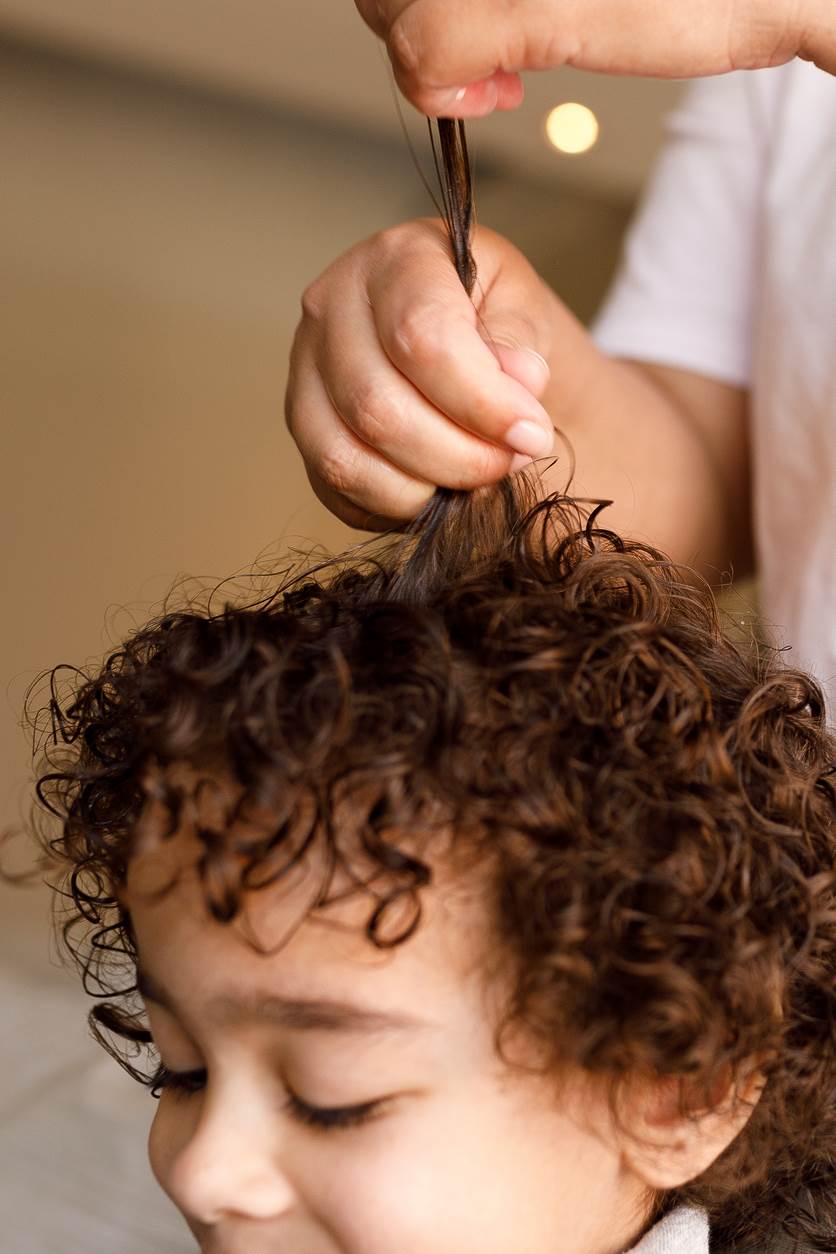 Aplicando creme de pentear em cabelo cacheado de criança.