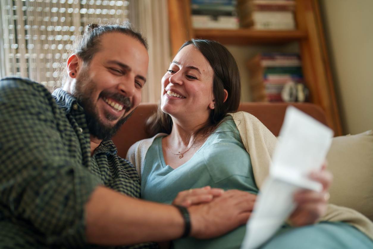 Casal sentado no sofá, conversando sobre o nome do bebê, lendo opções em uma lista, sorrindo.