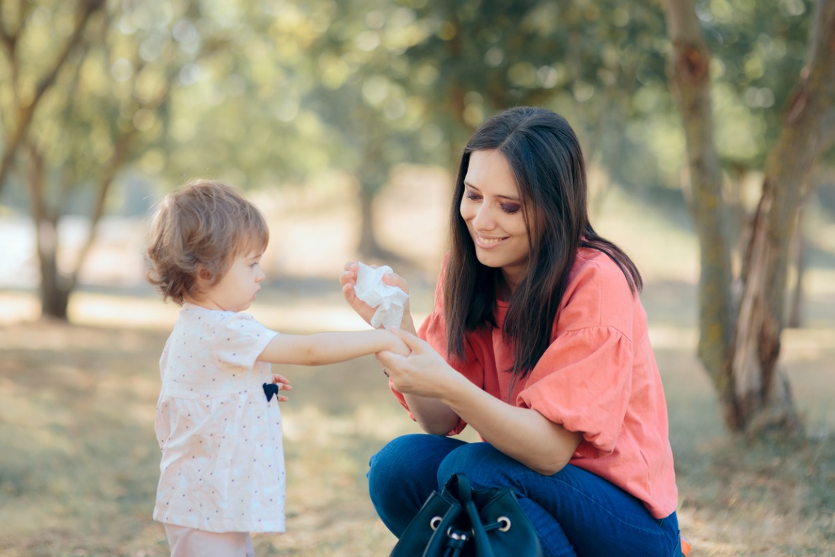 uma mãe limpando as mãos de seu filho pequeno com um lenço umedecido em um parque. 