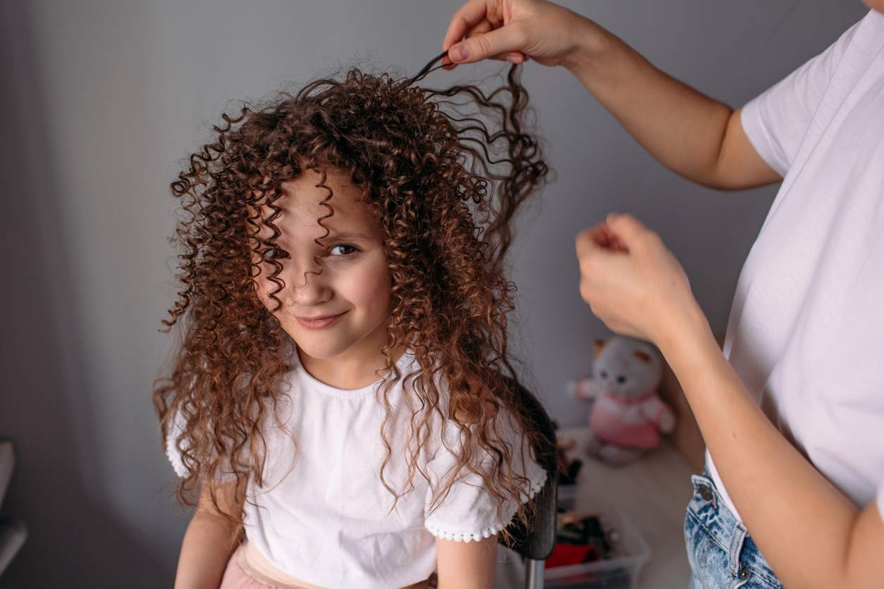 Aplicando creme de pentear em cabelo cacheado de menina.