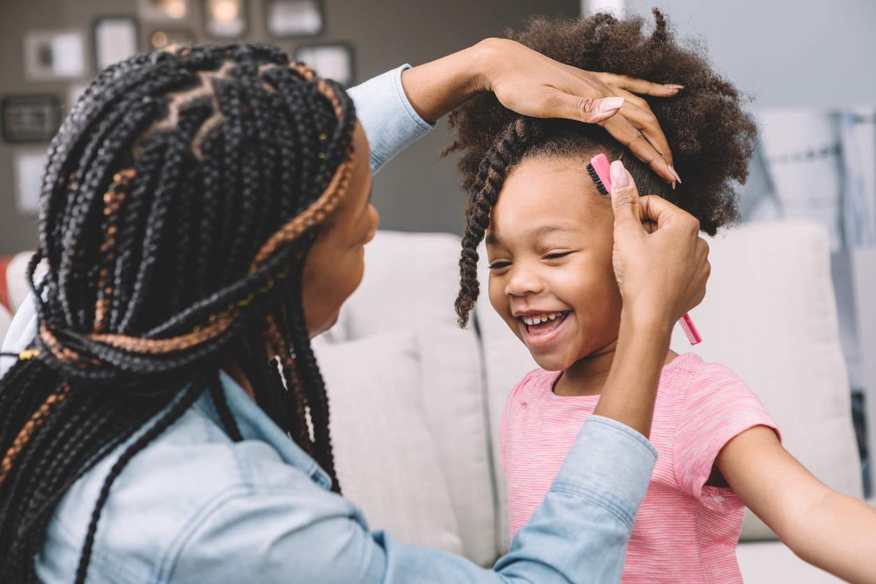 Mãe fazendo penteado no cabelo da filha sorridente.