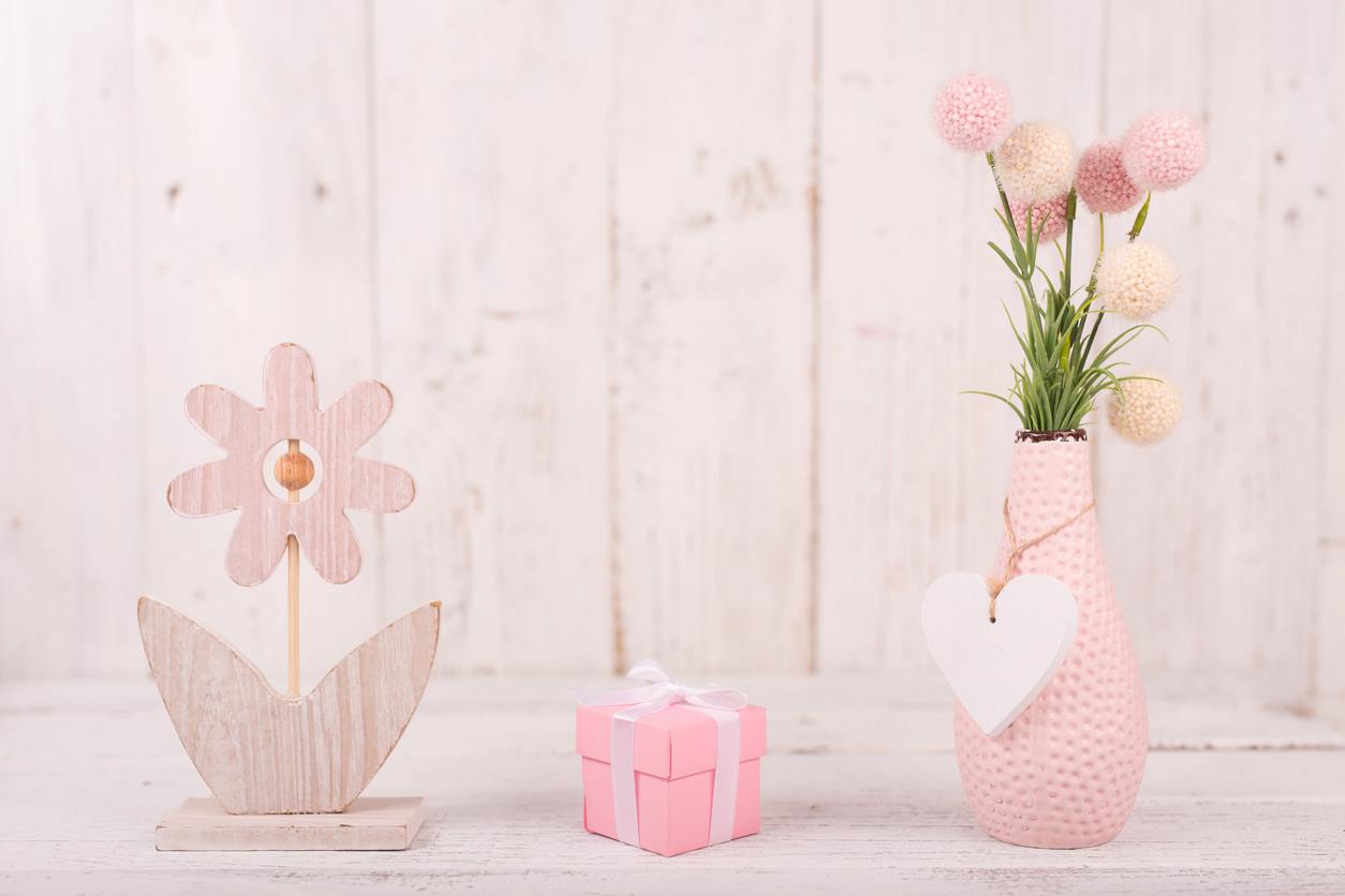 Mesa decorada com objetos em tom rosa, com destaque para garrafa que serve de vaso para flores de pompom.