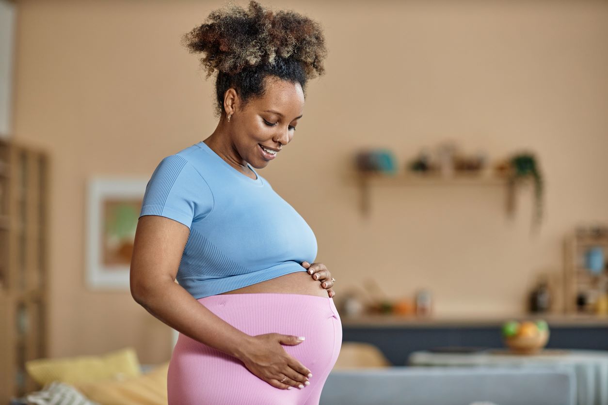 Mulher grávida sorrindo e segurando a barriga em casa.