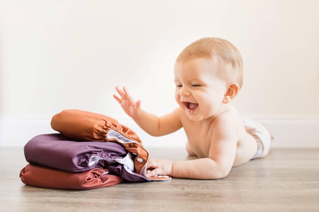 Bebê sorridente brincando com fraldas reutilizáveis 