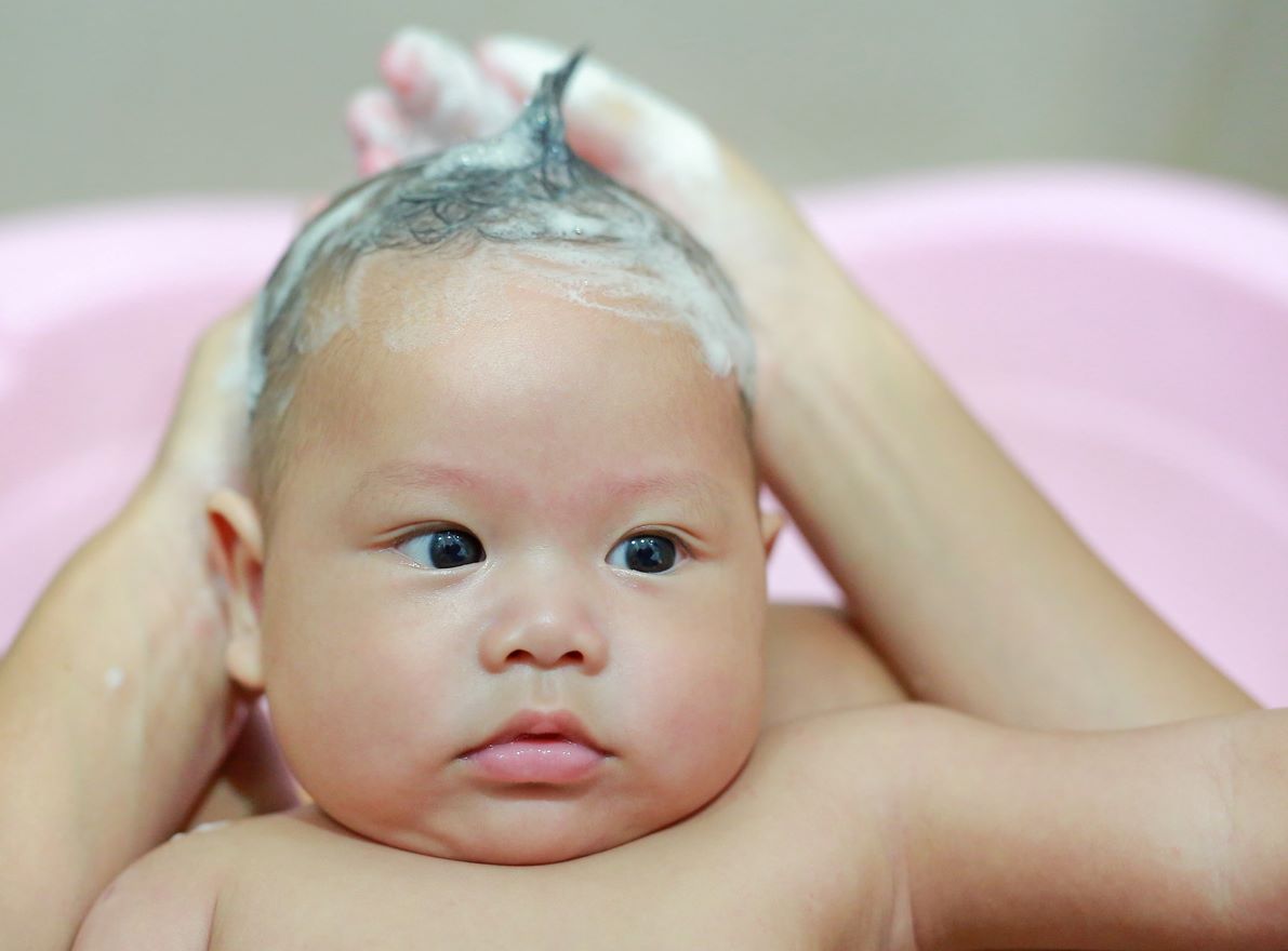 Bebê com o cabelo ensaboado durante o banho.