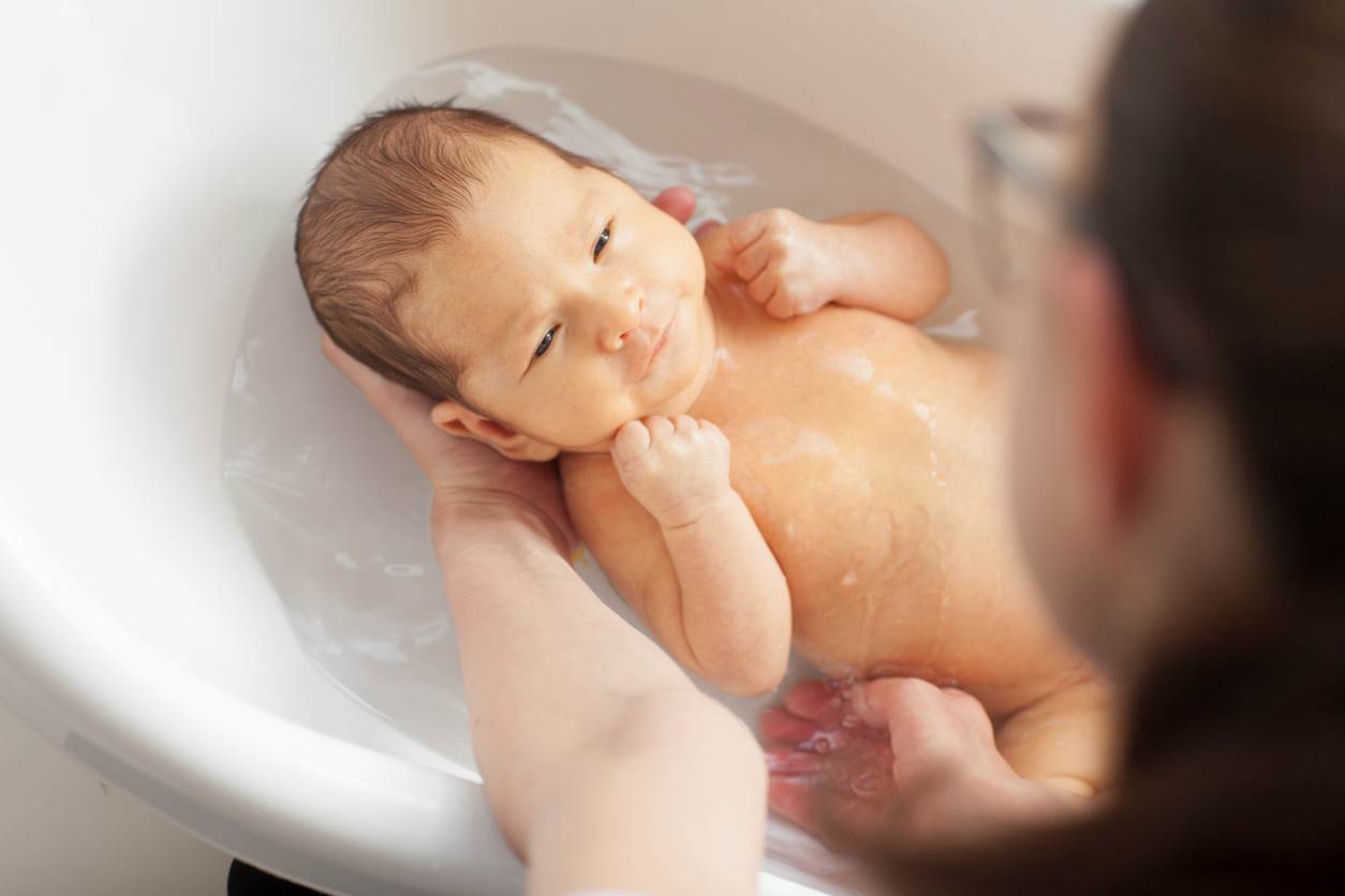 Bebê sendo banhado em uma banheira, relaxado e com expressão tranquila.