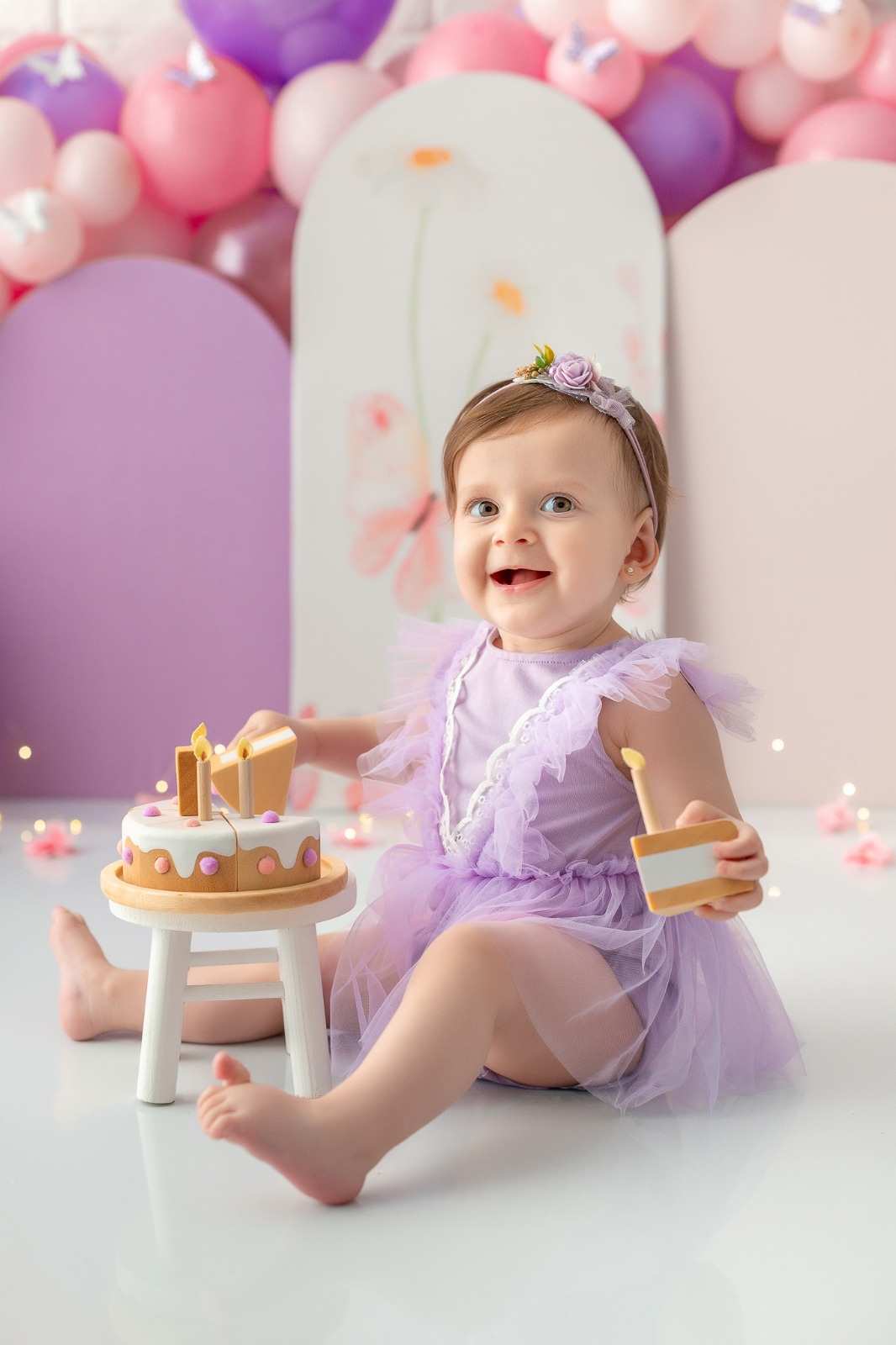 Menininha se divertindo com bolinho de madeira, em ensaio smash the cake, em cenário rosa e lilás.