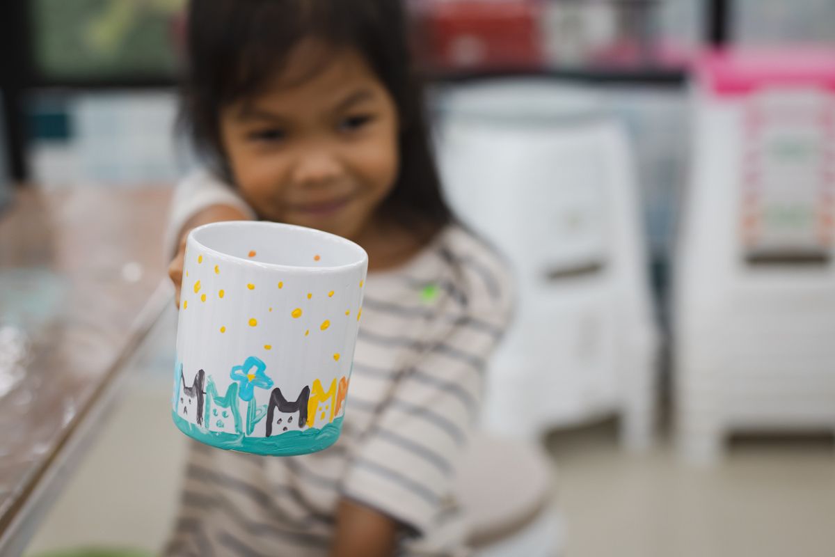 Criança segurando uma caneca decorada com desenhos de gatos e flores. 