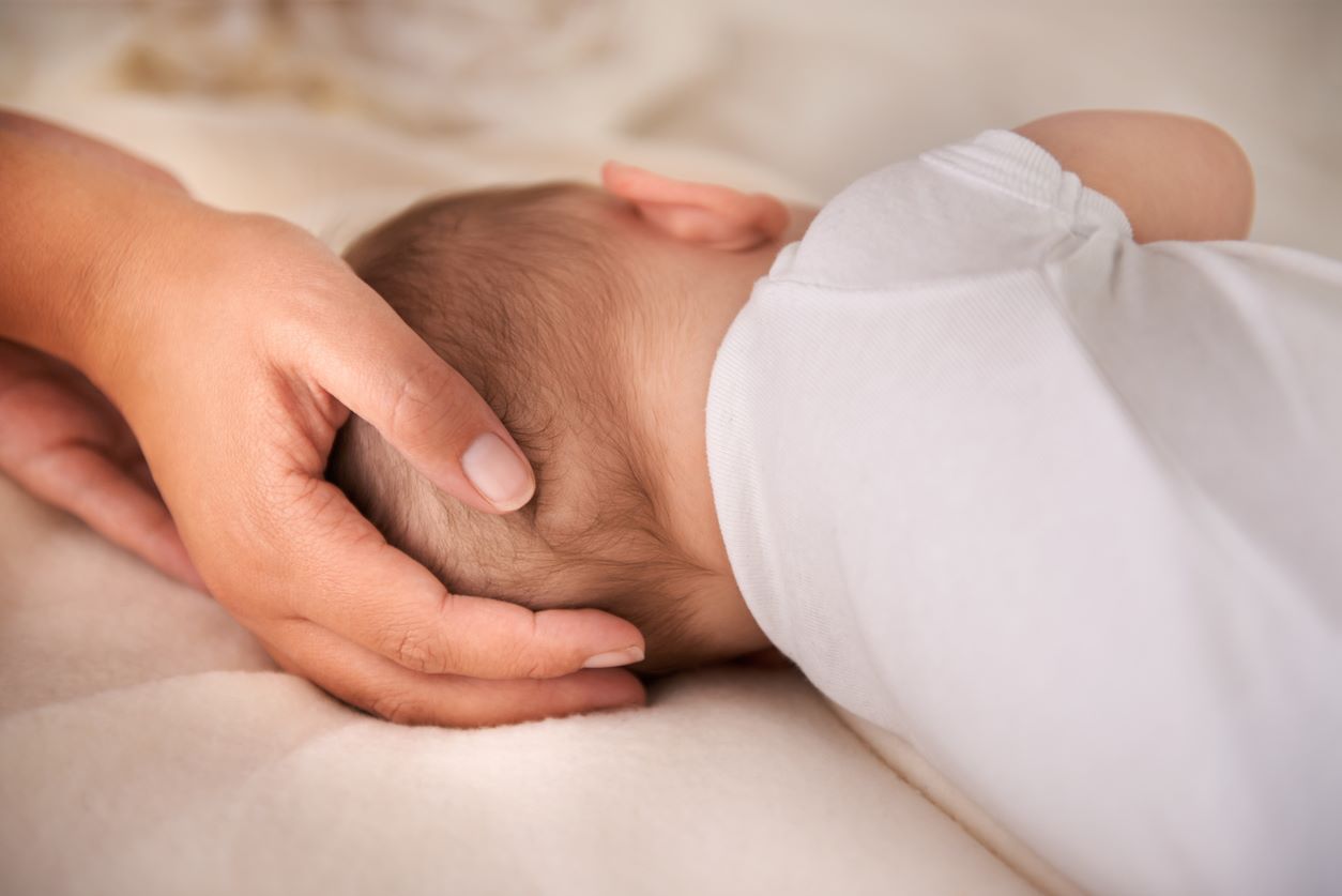 Mão acariciando a cabeça de um bebê deitado de bruços.