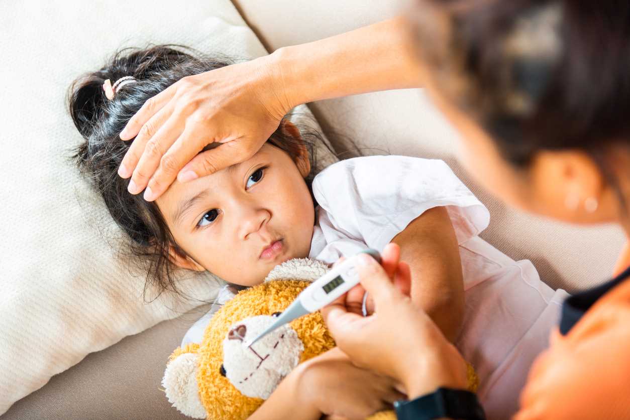 Adulto medindo a temperatura de uma criança doente com um termômetro digital enquanto toca a testa dela. 