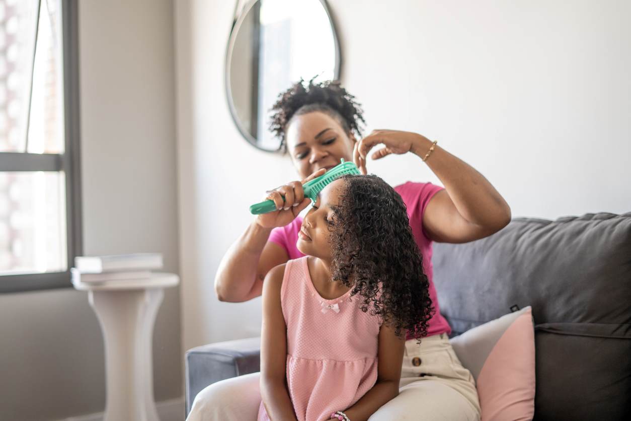 Mãe desfazendo pequenos nós no cabelo cacheado de sua filha.