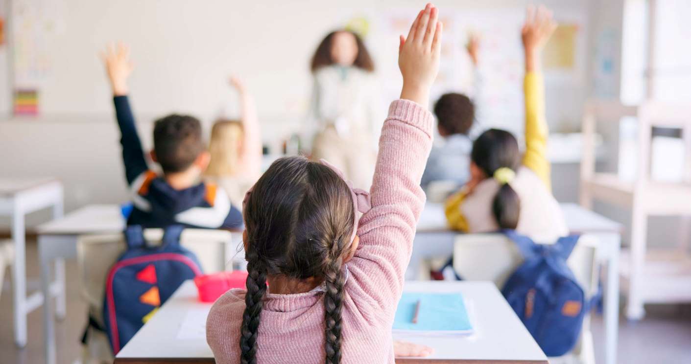 Crianças levantando a mão em sala de aula durante a aula.