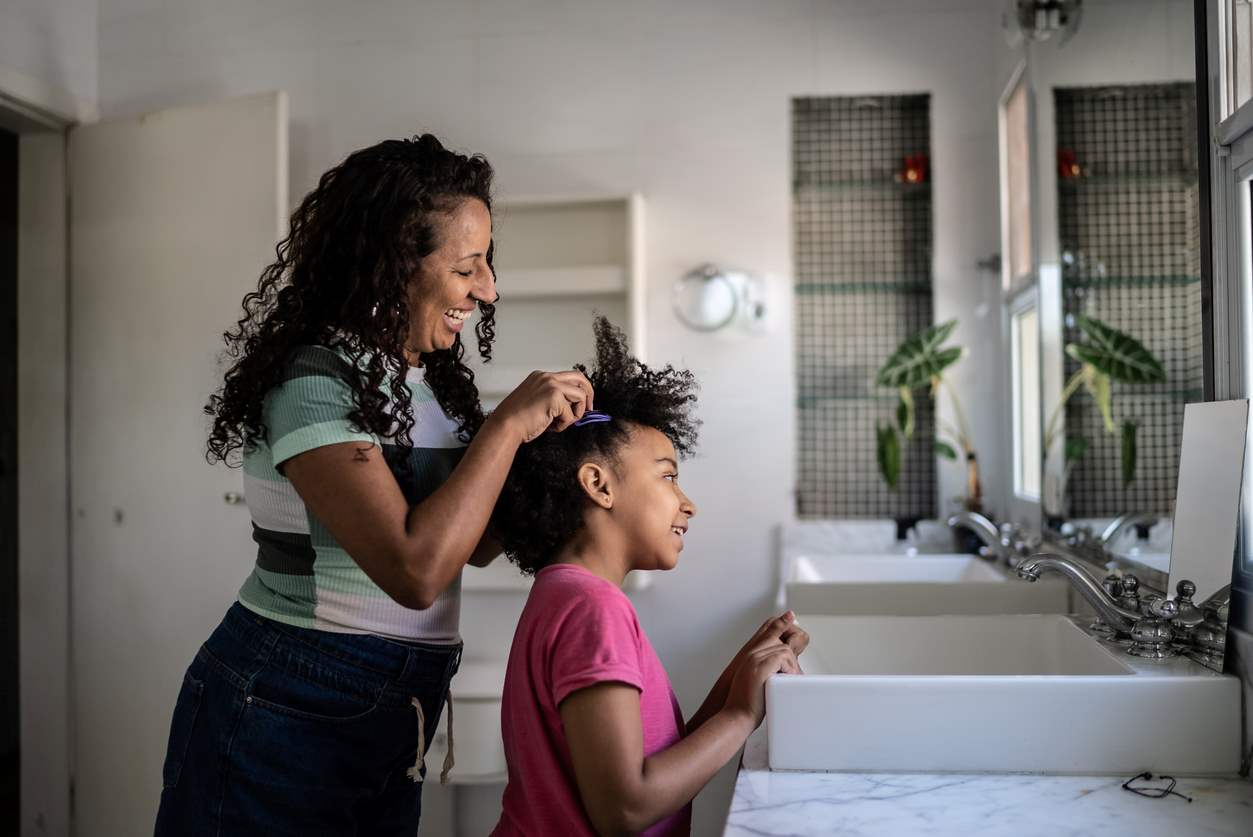 Mãe penteando o cabelo da filha no banheiro 